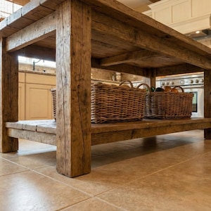 A rustic wooden kitchen island with a lower shelf. The island is constructed from thick, weathered wood, showcasing its natural grain and texture. Reclaimed Wood Kitchen Island , Farmhouse Rustic Kitchen Island Shelf, Counter Height Dining Table, butcher block island