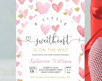 May include: A pink and gold baby shower invitation featuring a watercolour heart design. The text reads "A Little Sweetheart is on the Way" and includes the name Katherine Williams, date, time, and location of the event. RSVP information and a website address are also included.