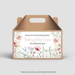 May include: A brown cardboard box with a handle, decorated with a floral design and a label that reads "Thank you so much for coming! Britteny's Baby Shower November 18th, 2024" and a website address.