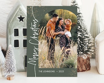 Könnte beinhalten: Eine grüne Weihnachtskarte mit einem Foto einer dreiköpfigen Familie, die auf einem Feld steht. Der Text "Merry Christmas" ist in weißer Schrift auf der linken Seite der Karte geschrieben. Der Text "THE JOHNSON'S - 2023" ist in weiß am unteren Rand der Karte geschrieben.