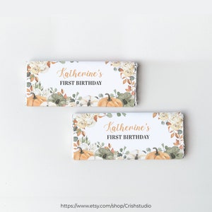 May include: Two white chocolate bar wrappers with a watercolor design of pumpkins, fall leaves, and flowers. The text on the wrappers reads "Katherine's First Birthday".
