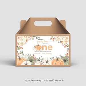 Può includere: Una scatola di cartone marrone con maniglia, decorata con un'etichetta bianca che presenta un'illustrazione ad acquerello di zucche, fiori e vegetazione. L'etichetta recita "La nostra piccola zucca compie un anno" e "Grazie mille per essere venuto al primo compleanno di Katherine".