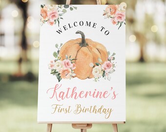 May include: Welcome to Katherine's First Birthday sign with a watercolor pumpkin and floral design. The sign is on an easel.