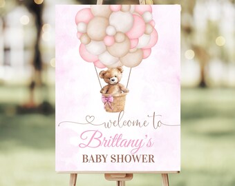 Puede incluir: Un cartel de bienvenida para una baby shower rosa y marrón con un osito de peluche en un globo aerostático hecho de globos rosas y marrones. El cartel dice "Bienvenido a la baby shower de Brittany".