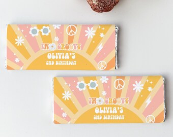 May include: Two yellow and pink chocolate bar wrappers with a groovy 70s theme. The wrappers feature a sunburst design with peace signs, flowers, and sunglasses. The text on the wrappers reads "The Groovy Olivia's 2nd Birthday".
