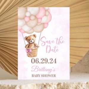 May include: A baby shower invitation featuring a teddy bear in a hot air balloon made of pink and beige balloons. The invitation includes the text "Save the Date", the date 06.29.24, and "Brittany's BABY SHOWER". The background is a soft pink watercolor.