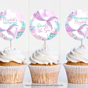 Pu&ograve; includere: Tre cupcake decorati con topper a tema sirenetta. I topper presentano una coda di sirena rosa e viola, conchiglie e il testo "Elizabeth's First Birthday", "Under the Sea" e "Happy Birthday Elizabeth".