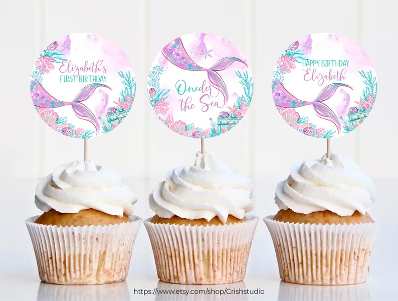 Pu&ograve; includere: Tre cupcake decorati con topper a tema sirenetta. I topper presentano una coda di sirena rosa e viola, conchiglie e il testo "Elizabeth's First Birthday", "Under the Sea" e "Happy Birthday Elizabeth".