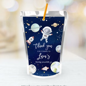 May include: A blue and white juice pouch with a space-themed design. It features an astronaut, planets, stars, and a rocket. The text on the pouch reads "Thank you for coming to Luca's First trip around the sun".