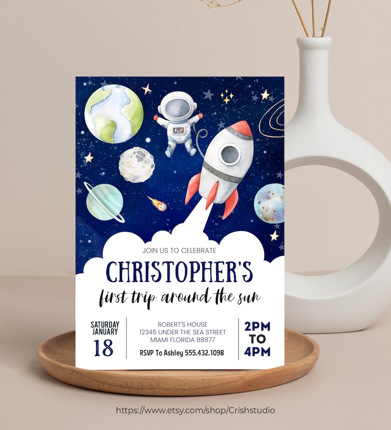 May include: A blue and white astronaut and rocket ship on a dark blue background with stars and planets. The text "JOIN US TO CELEBRATE CHRISTOPHER'S first trip around the sun" is at the top of the invitation. The text "SATURDAY JANUARY 18" is on the left side of the invitation. The text "ROBERT'S HOUSE 12345 UNDER THE SEA STREET MIAMI FLORIDA 88877 RSVP To Ashley 555.432.1098" is on the right side of the invitation. The text "2PM TO 4PM" is at the bottom of the invitation.