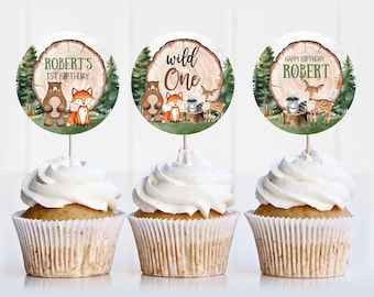 May include: Three round cupcake toppers with woodland animal illustrations and text. The toppers feature a brown bear, fox, raccoon, deer, and a tree stump with the text "Wild One" and "Robert's 1st Birthday".