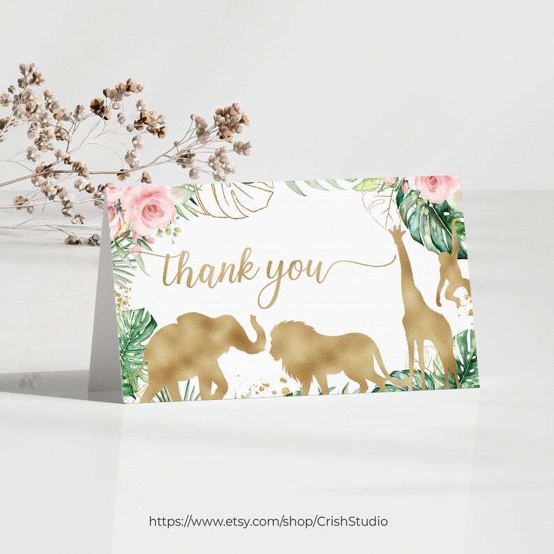 May include: A folded thank you card with a gold safari animal design. The card features an elephant, lion, and giraffe, with the words "thank you" in gold script. The card is decorated with pink roses and green leaves.