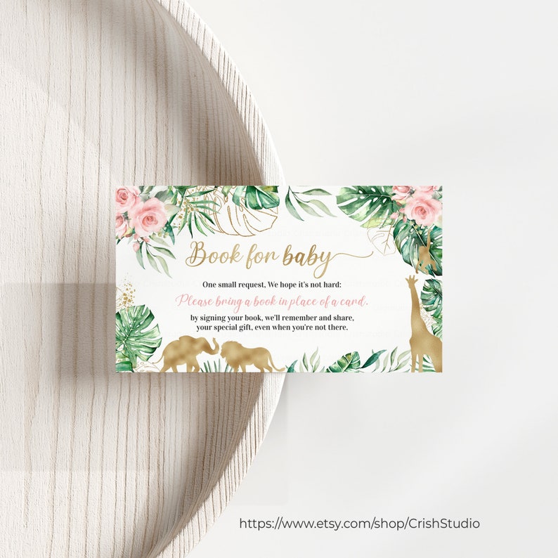 May include: A baby shower invitation card with a safari theme. The card features gold text that reads "Book for baby" and includes illustrations of a giraffe and elephants. The card is decorated with pink roses and green leaves.