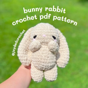 May include: A beige crochet bunny rabbit with long floppy ears, black eyes, and pink cheeks. The text "bunny rabbit crochet pdf pattern" is written in white script. The Instagram handle @jaydedorochet is also visible.