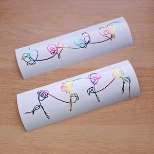 May include: Two white vinyl stickers with holographic rainbow designs. One sticker features three connected hearts, and the other has three connected flowers. The designs are outlined in black.