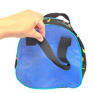 Puede incluir: Una bolsa de deporte redonda con un panel circular azul vibrante, laterales de tela negra con un patr&oacute;n abstracto colorido y correas de nailon negro. La bolsa est&aacute; acentuada con ribetes de color verde azulado brillante en los bordes y un asa superior.
