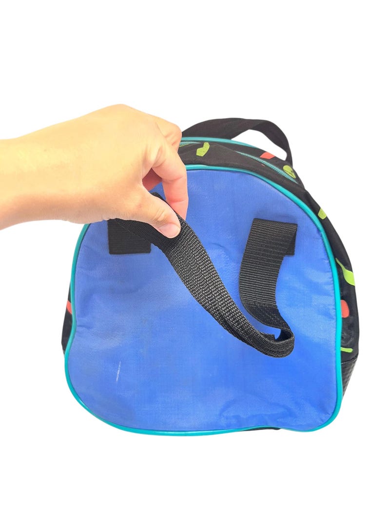 Puede incluir: Una bolsa de deporte redonda con un panel circular azul vibrante, laterales de tela negra con un patr&oacute;n abstracto colorido y correas de nailon negro. La bolsa est&aacute; acentuada con ribetes de color verde azulado brillante en los bordes y un asa superior.