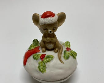 May include: A small ceramic Christmas trinket box featuring a brown mouse wearing a red Santa hat, sitting on a white base with green holly leaves and red berries.