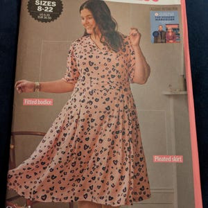 May include: A sewing pattern for a "PLEATED DRESS" showing a woman in a pink dress with black heart patterns. Sizes are 8-22 (US 6-20, EUR 36-50). The dress has a fitted bodice and pleated skirt. Includes a pattern from "THE MODERN WARDROBE".