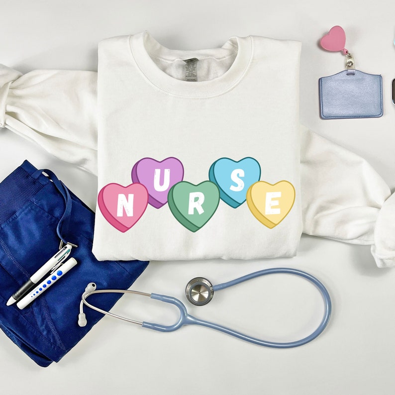 Sport Grey crewneck  sweater folded lying on floor. Sweater has 5 candy hearts with the letters stating "NURSE"