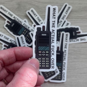 Può includere: Un adesivo bianco e nero con un'illustrazione di un walkie-talkie di cartone animato e il testo "What the actual fuck, over".