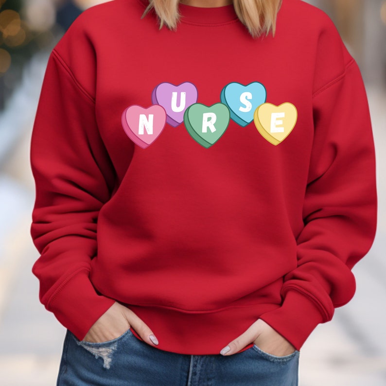 Woman wearing a red crewneck sweater. Sweater has 5 candy hearts with the letters stating "NURSE"