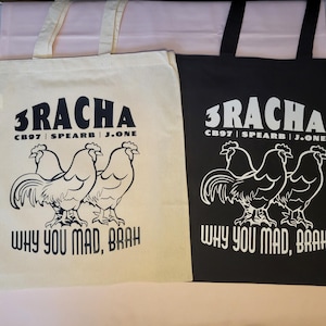 May include: Two tote bags, one cream and one black, with the text "3RACHA" above a rooster graphic. Below the graphic is the phrase "WHY YOU MAD, BRAH". The bags have black handles.