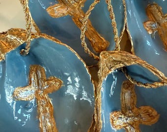 May include: Close-up of several blue shell ornaments with gold trim and a gold cross in the center. Each ornament is suspended by a gold rope. The ornaments have a glossy finish.