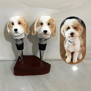 Può includere: Due tappi per bottiglie a forma di testa di cane, bianchi e marroni, con una base marrone. Una foto di un cane bianco e marrone è sullo sfondo.