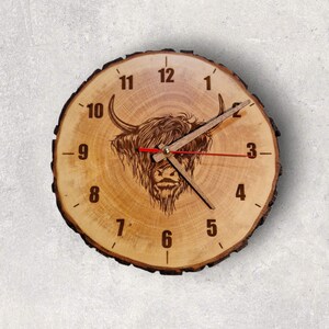 Könnte beinhalten: Eine rustikale Holzuhr mit einem geschnitzten Bild einer Highland-Kuh mit braunem Fell. Das Zifferblatt der Uhr hat schwarze römische Ziffern und schwarze Zeiger.