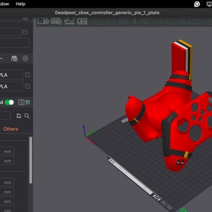 May include: A 3D printed model of a red and black Xbox controller with a Deadpool design. The model is shown on a grey platform with a grid pattern. The model is being prepared for 3D printing using a software program.