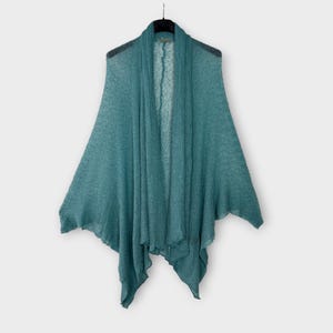 May include: A teal open-front shawl hangs on a black hanger. The lightweight fabric drapes gracefully, creating a layered effect. The shawl's design features a wide, open front and flared sleeves, ideal for layering. The colour is a muted teal.