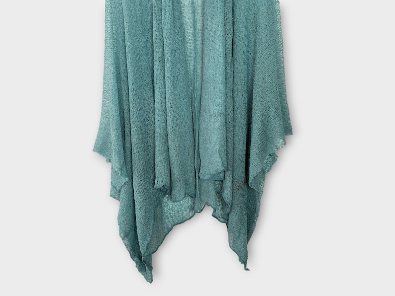 May include: A teal-coloured, open-front cardigan with a textured knit. The lightweight garment has a draped design with asymmetrical edges. The fabric appears soft and flowing, suitable for layering.
