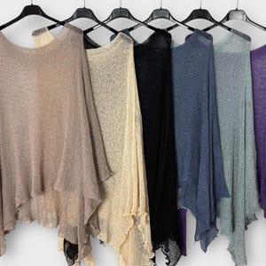 Könnte beinhalten: Eine Auswahl an leichten Ponchos in verschiedenen Farben, darunter Beige, Creme, Schwarz, Blau, Grau und Lila, hängen an schwarzen Kleiderbügeln. Die Ponchos haben einen fließenden, asymmetrischen Schnitt mit einem gewellten Saum.