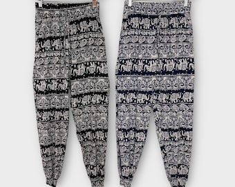 May include: Two pairs of black and white elephant print trousers with elastic waistbands. The trousers are hanging on wooden hangers.