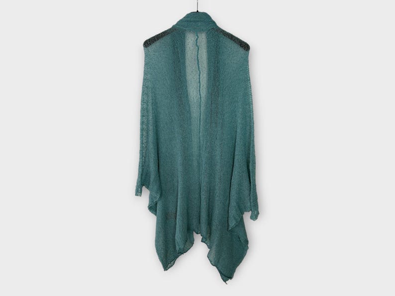 May include: A teal open-front cardigan hangs on a black hanger against a white background. The lightweight knitwear features a draped design with a shawl collar and long sleeves. The fabric appears to be semi-sheer.