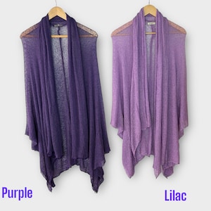 May include: Two draped, open-front cardigans in shades of purple and lilac hang on wooden hangers. The purple cardigan is a deep shade, while the lilac one is a lighter hue. The word "Purple" and "Lilac" are written below the cardigans.