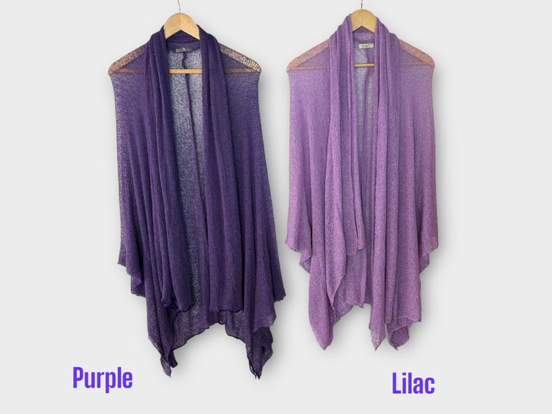 May include: Two draped, open-front cardigans in shades of purple and lilac hang on wooden hangers. The purple cardigan is a deep shade, while the lilac one is a lighter hue. The word "Purple" and "Lilac" are written below the cardigans.