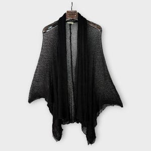 May include: A black, open-front cardigan with a draped design, hanging on a wooden hanger. The lightweight knit fabric has a slightly sheer appearance. The cardigan's sleeves extend to the elbows, and the hemline falls to the mid-thigh.