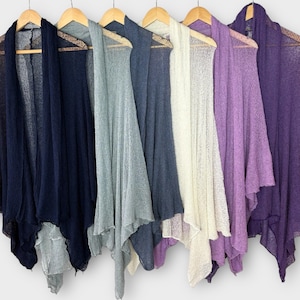 以下が含まれることがあります： ネイビー、グレー、オフホワイト、紫など、さまざまな色のオープンフロントカーディガンが木製のハンガーに掛けられています。 カーディガンは、軽量で透け感のあるテクスチャとドレープデザインです。