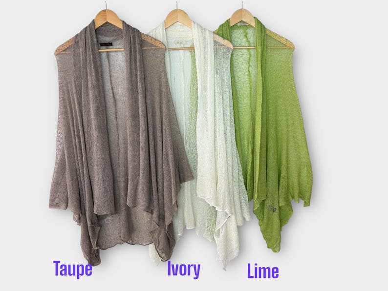May include: Three open-front cardigans in taupe, ivory, and lime green hang on wooden hangers. The lightweight, sheer fabric drapes loosely. The colors are labeled below the cardigans.