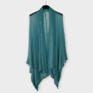 May include: A teal open-front cardigan hangs on a black hanger. The lightweight knit fabric drapes loosely, creating a flowing silhouette. The cardigan has a shawl collar and a slightly asymmetrical hemline, suitable for layering.
