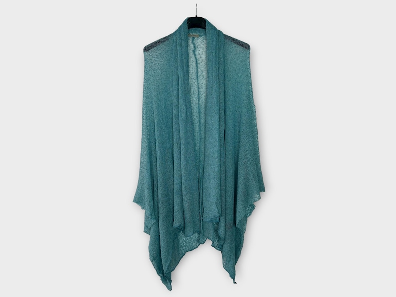 May include: A teal open-front cardigan hangs on a black hanger. The lightweight knit fabric drapes loosely, creating a flowing silhouette. The cardigan has a shawl collar and a slightly asymmetrical hemline, suitable for layering.