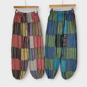 Può includere: Due paia di pantaloni patchwork a righe colorate con vita a coulisse. I pantaloni sono realizzati con una varietà di tessuti e colori, tra cui rosso, verde, blu e giallo.