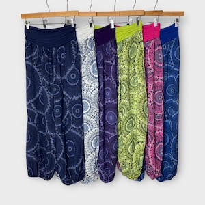 Op de afbeelding: Zes paar bedrukte broeken hangen aan een houten rek. De broeken zijn allemaal in verschillende kleuren en hebben een cirkelvormig patroon. De broeken zijn gemaakt van een zachte, comfortabele stof en zijn perfect voor casual wear.