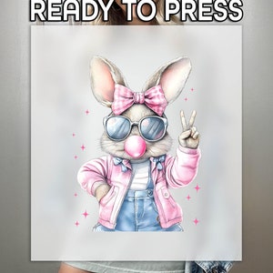 May include: A pink and grey cartoon bunny wearing sunglasses and a pink jacket with a peace sign. The bunny has a pink bow and is blowing a bubble.