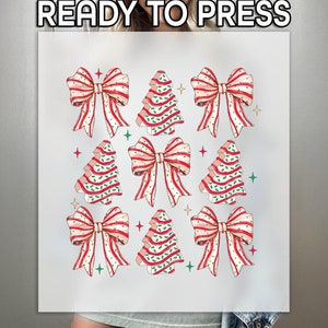 May include: A white t-shirt with a design of nine red and white striped bows and nine green and white striped Christmas trees. The text "READY TO PRESS" is at the top of the shirt.
