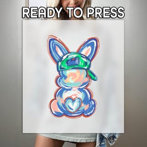 May include: A white canvas with a colorful illustration of a bunny wearing a green cap. The bunny is primarily blue, with accents of orange, pink, and white. The text "READY TO PRESS" is at the top.