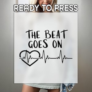 May include: White iron-on transfer with black text that reads "The Beat Goes On" and a black heart with a heartbeat line.