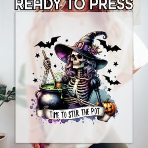 May include: A white t-shirt with a colorful illustration of a skeleton witch stirring a cauldron with a wooden spoon. The witch is wearing a purple and black dress and a black witch hat with a purple ribbon. The text "Time to Stir the Pot" is written on a banner below the cauldron.